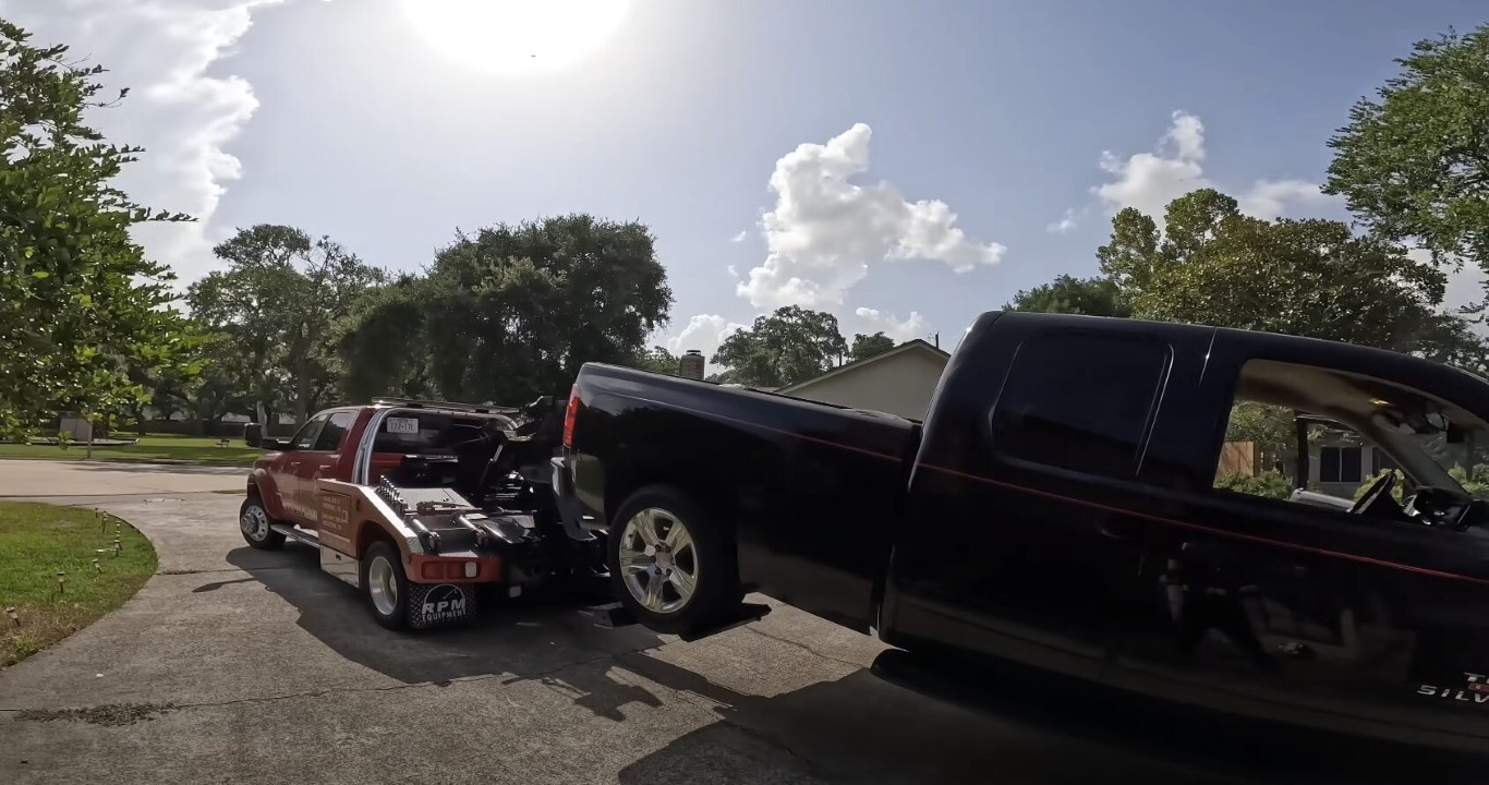 Red heavy duty tow truck hauling a large black pickup truck on a residential street in Islip, NY