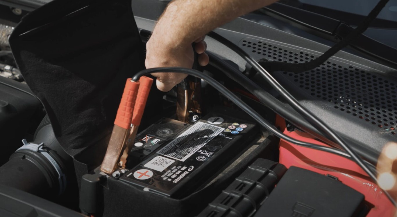 Mechanic attaching red and black jumper cables to a car battery for a jump start service in Islip, NY