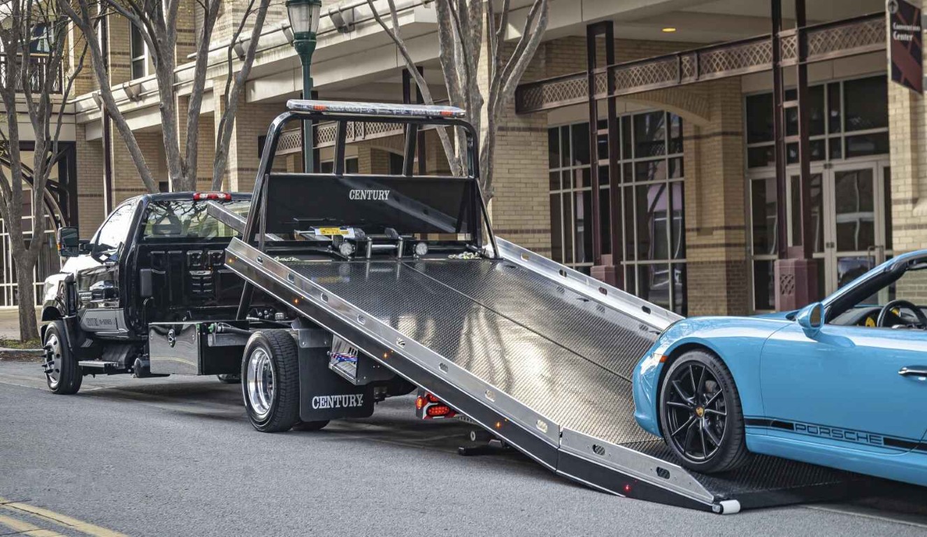 Black flatbed tow truck lowering its ramp to load a Porsche for specialized vehicle transport