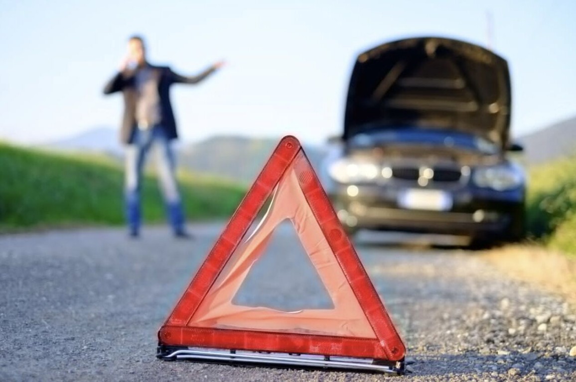 Driver stranded on the road with a broken down car and a warning triangle, calling for lockout help